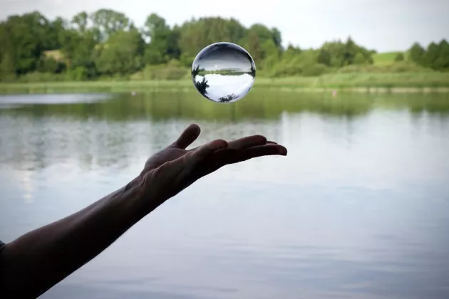 hand bouncing a water ball with a lake and trees in the background
