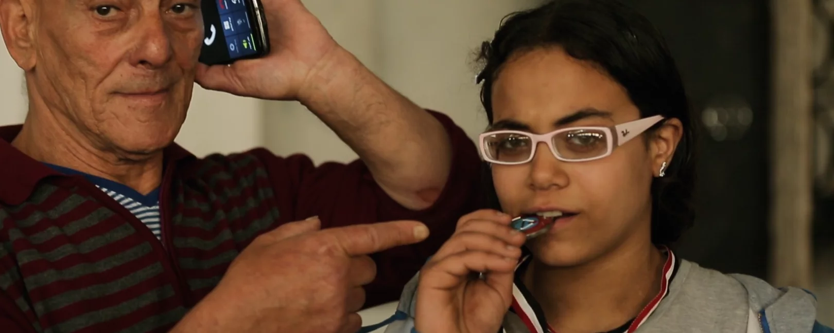 Girl biting on a medal with her coach beside her talking on the phone 